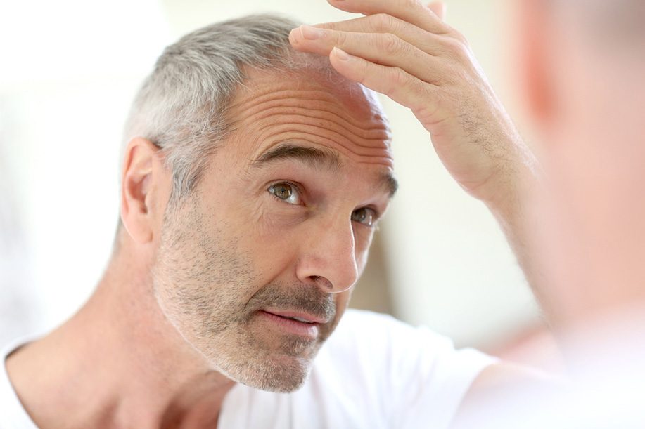Mature man looking at hair in mirror.