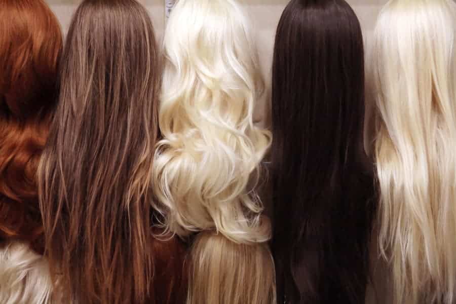 Five wigs in various colors displayed in a row on wig forms