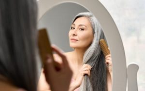 Person combing long, gray hair in oval mirror